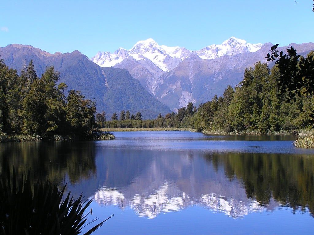 Snowcapped peaks of the Southern Alps reflected in the calm waters of Lake Matheson near Fox Glacier.